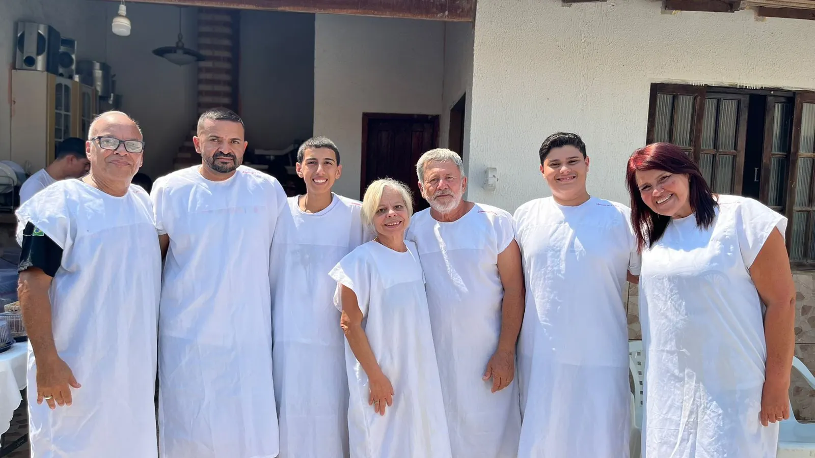 Sete pessoas de túnica branca sorrindo antes do batismo nas águas